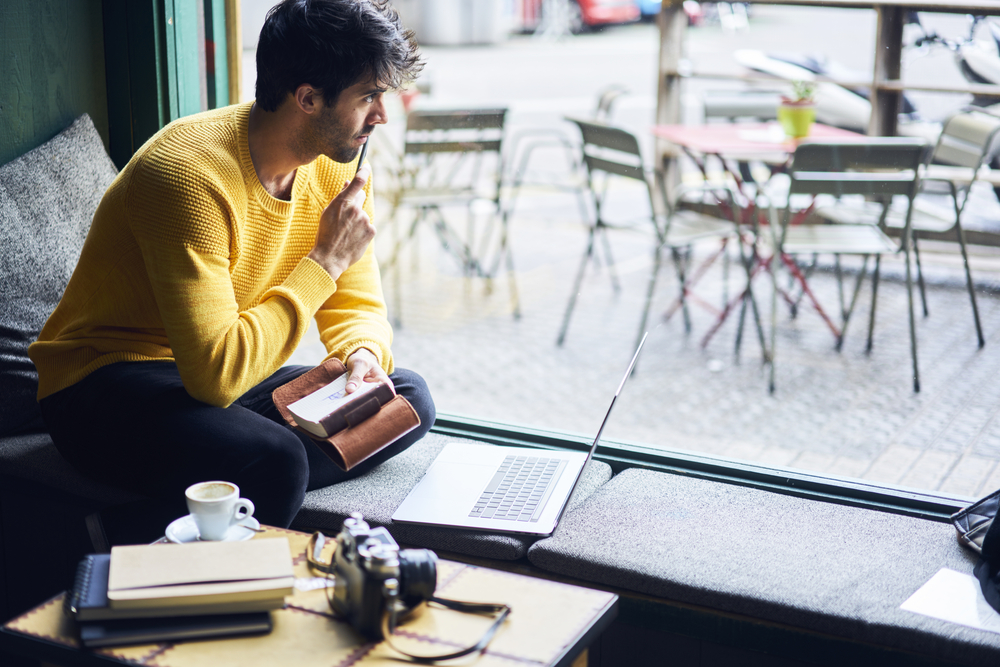 一个男人坐在咖啡店里，手里拿着笔记本电脑和笔记本电脑